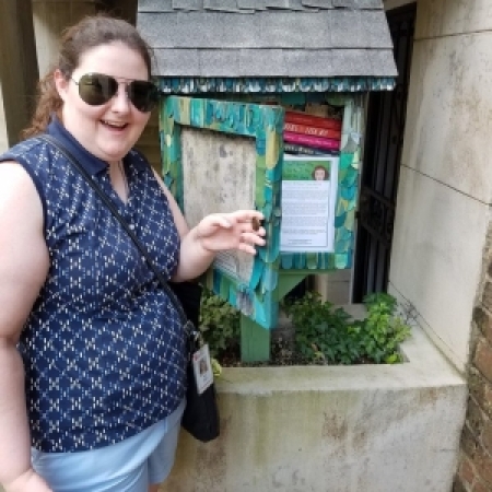 30s woman with sunglasses standing in front of a little free library