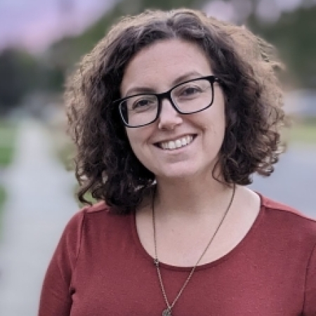 Photo of a white woman with curly hair and black glasses smiling at the camera